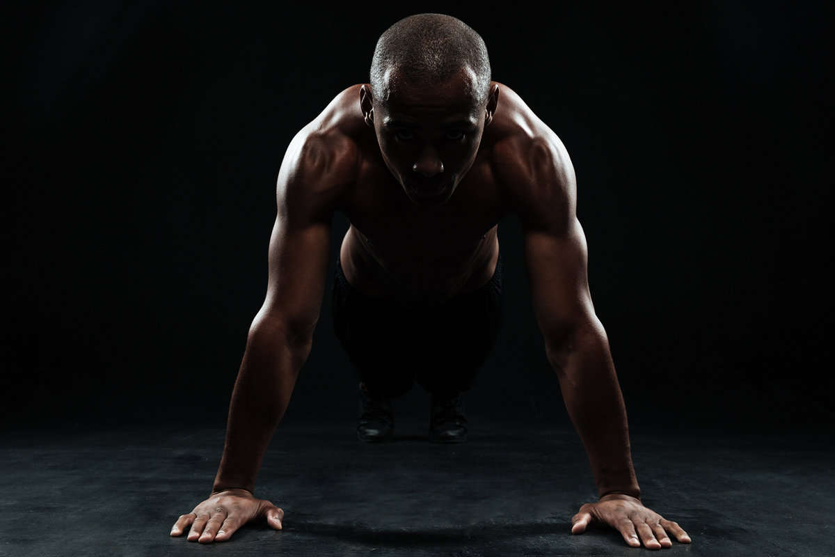 Portrait of youg afro american sports man doing pushup exercise, on black background